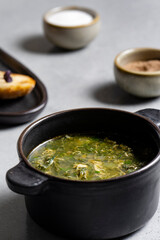 Soup with green sorrel in black ceramic pot on gray background