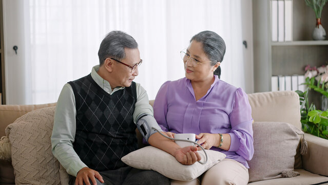 elderly asian grandmother checking blood pressure for grandfather with digital Measuring portable device at home with.asian couple checking blood pressure at home.support empathy together concept