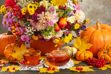 Autumn bouquet with aster pumpkins and yellow leaves. Tea in glass. The concept of autumn still life with tea