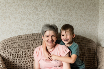 a little boy and his grandmother are sitting on the couch and laughing. caring for loved ones. old age and youth. family relationships