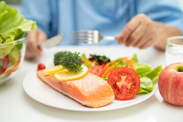 Asian elderly woman patient eating salmon steak breakfast with vegetable healthy food in hospital.