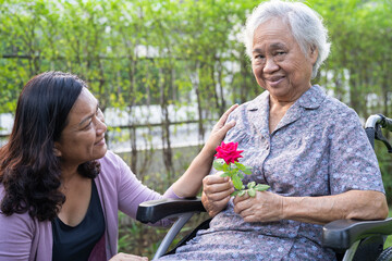 Caregver help Asian elderly woman holding red rose flower, smile and happy in the sunny garden.