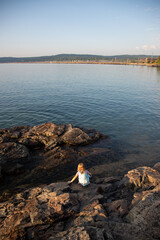 Girl crouching at edge of lake at sunrise, Lake Superior