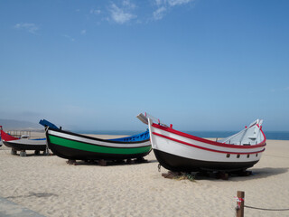sets of two antique fishing boats on the beach of Nazaré, Portugal. Restored painting. nice sunny day with the sea in the background.
