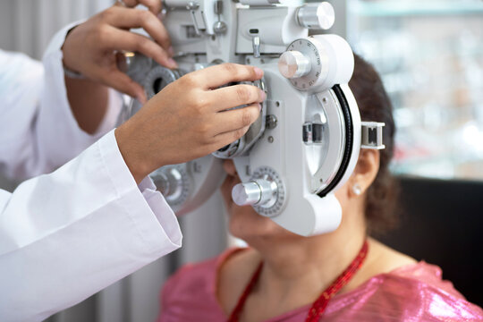 Optometrist's hand adjusting Phoropter for middle-aged Indian or Nepalese woman during eye examination, diagnostic ophthalmology
