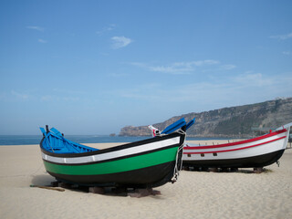 Naklejka na ściany i meble sets of two antique fishing boats on the beach of Nazaré, Portugal. Restored painting. nice sunny day with the sea in the background.