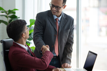 Indian senior businessman handshake with young businessman at desk, congratulations on your success and new position