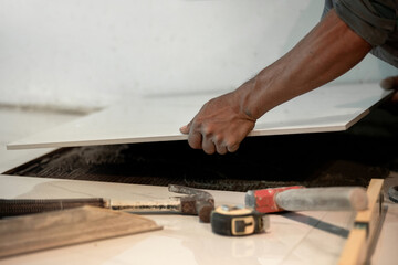Laying ceramic tiles, close up hands of the worker are laying the ceramic tile on the floor