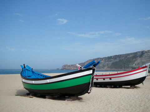 sets of two antique fishing boats on the beach of Nazaré, Portugal. Restored painting. nice sunny day with the sea in the background.