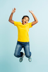 Portrait of excited African boy in casual clothes, hands up jumping, isolated on blue background