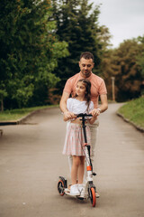 Dad with daughter in park teaching to ride scooter