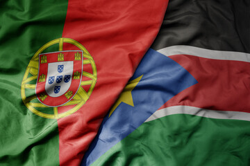 big waving national colorful flag of portugal and national flag of south sudan .