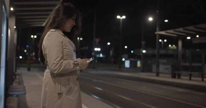 Medium Shot of Young Professional Latin Woman Texting on Empty Urban Street at Night