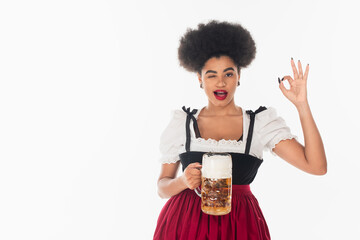 african american oktoberfest waitress with mug of craft beer winking and showing okay sign on white