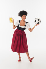 african american oktoberfest waitress with mug of foamy beer playing football on white, full length