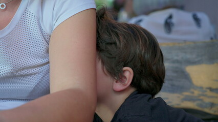 Bored child hiding behind mother's arm feeling boredom, close-up of shy kid with nothing to do