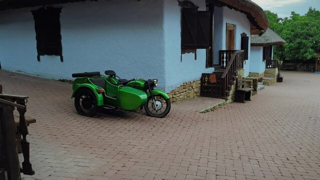 Exploring the Restored Old Village: A Classic Green Motorcycle with a Sidecar Adds a Touch of Adventure to the Picturesque Landscape.