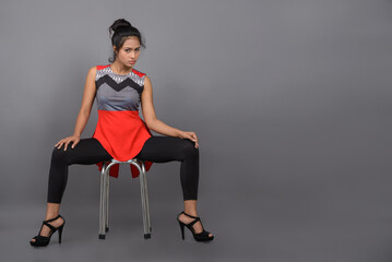 Studio shot of a young, beautiful Indian female model in casual wear wearing red and grey designer top and blue jeans against grey background. Female model. Fashion Portrait.