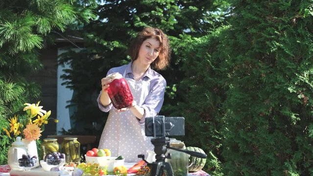 A woman shoots a video on a smartphone, compotes for the winter. On a warm autumn day, a housewife leads a video blog, teaches her subscribers how to preserve berries and fruits, and shows a jar with