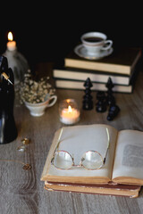 Fototapeta na wymiar Vintage books, reading glasses, gold pen, hand model, gold jewelry, scented candles, flowers, chess pieces and cup of tea or coffee on the table. Dark academia concept. Selective focus.