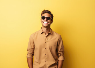 Obraz premium Portrait of a diverse man wearing sunglasses, smiling and posing confidently against a solid yellow backdrop.