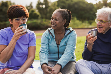 Multiracial senior friends drinking hot tea together after yoga class at park