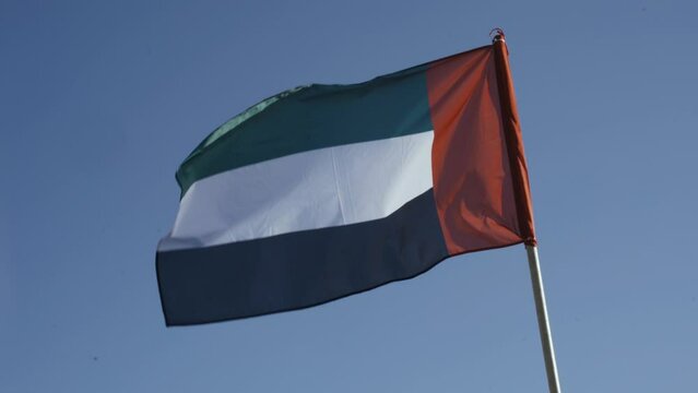 Flag of the United Arab Emirates, fluttering against the blue sky. Close-up.