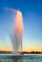 A rainbow forms at the top of the spray from the fountain in Fountain Hills Arizona at dusk with a full moon - 644557551