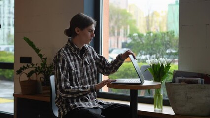 Side view serious young man checking time on watch walking away with laptop. Portrait of confident Caucasian concentrated freelancer leaving cafe in urban city indoors