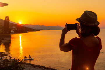 Fototapeta premium Silhouette of a woman taking a photo at sunset at Shkoder lake in Shiroka municipality, summer vacation. Albania