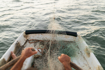 View from behind of sailor in small rickety boat rowing by hand while releasing net into sea for fishing