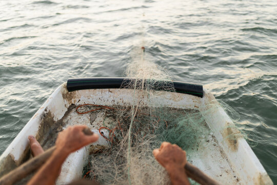 View from behind of sailor in small rickety boat rowing by hand while releasing net into sea for fishing