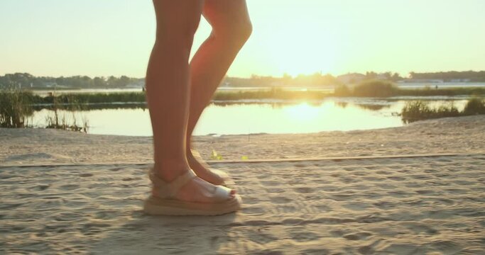 Women's feet in sandals walk along river embankment. Early morning, sunrise, sunbeams. Follow, side view, gimbal