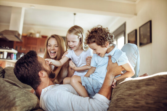 Happy Young Family Being Playful And Having Fun On The Couch In The Living Room At Home