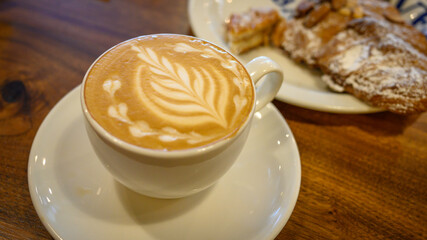 Cappuccino with artistic leaf-shape decoration in a white cup with almond croissant 
