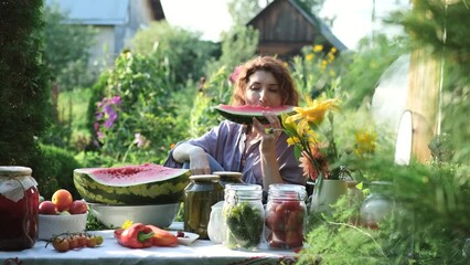Beautiful woman eating watermelon while sitting at the table in her summer cottage on a sunny day