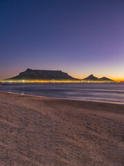 Fototapeta premium Vertical shot of Cape Town city lights with and table mountain loin's head in the background, Cape Town, South Africa
