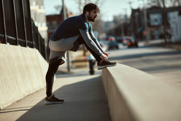 Young man tying his shoelaces while out jogging and exercising in the city