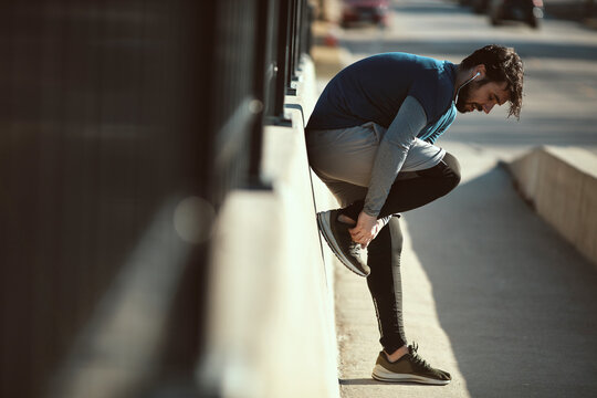 Young man tying his shoelaces while out jogging and exercising in the city