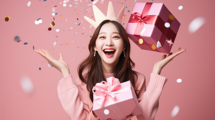 Happy brunette girl holding gift box and looking at the camera while enjoys over pink background