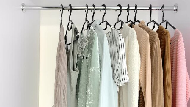 A woman chooses an outfit from a closet with stylish clothes. Women's wardrobe sweatshirts, shirts and blouses in neutral light colors. Concept: organization of the perfect order in the wardrobe
