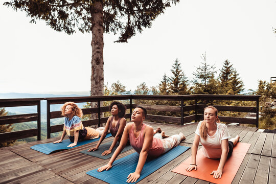 Young and diverse group of female friends doing yoga on a balcony of a cabin house in nature