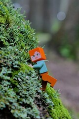 Obraz premium LEGO Minecraft figure of main character Alex climbing on forest rock densely covered with moss and lichen.