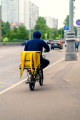 A food delivery man with a yellow backpack rides on the sidewalk on an e-bike