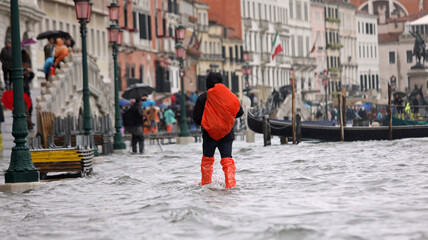 High tide in Venice Island in Italy and tourist with red backpack and leggings in the middle of the...