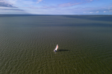Aerial drone shot of a sailboat healed over with a bright colourful gennaker or asymmetric spinnaker headsail in windy conditions under blue sky in The Netherlands. Empty vast blue water, ocean , lake