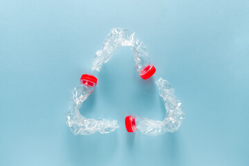 Three blue plastic water bottles bent together to form a recycling symbol on a blue background