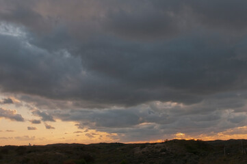 View on a dune landscape with a cloudy sky at sunset