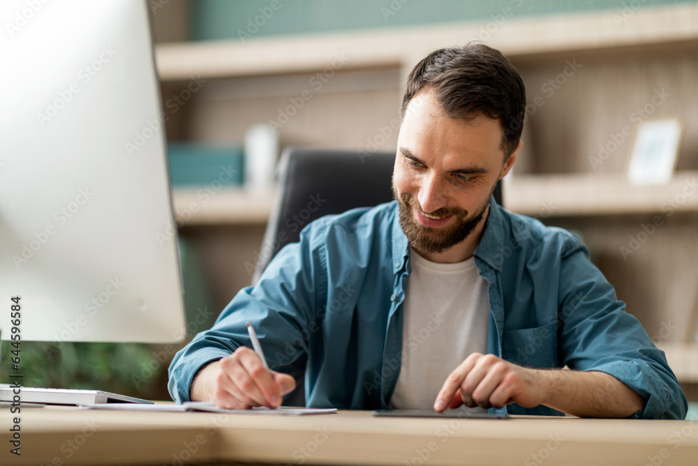 Aufkleber Smiling Businessman Using Digital Tablet And Taking Notes To Notebook In Office