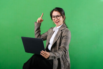 Smiling Asian business woman using laptop hand pointing up isolated on green background